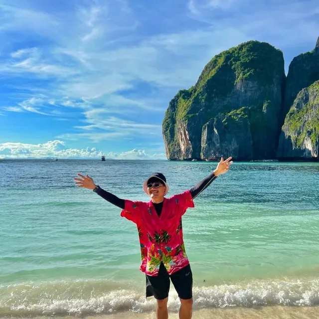 Tommy at the shore, arms outstretched, with limestone cliffs behind him