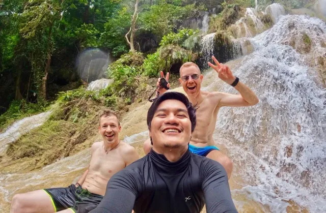 Tommy smiling with two travellers beside flowing water